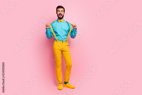 Full length body size view of his he nice attractive cheerful cheery funky guy wearing mint shirt yellow pants clothes pulling suspenders having fun isolated on pastel pink color background