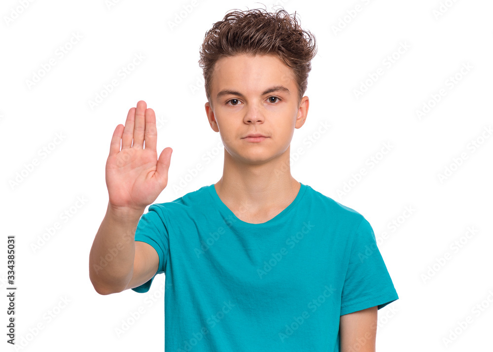 Teen boy doing stop sign with palm of hand, isolated on white background. Beautiful caucasian teenager making stop gesture with negative and serious facial expression. Serious child looking at camera.