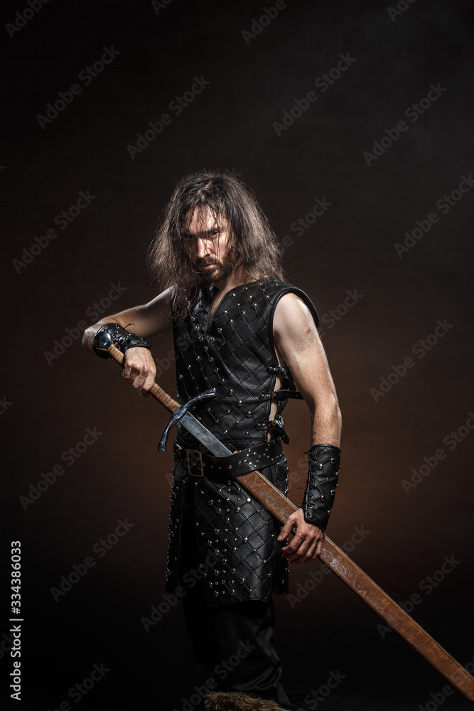 Man dressed in medieval armour and raincoat with longs word over smoke background. Courage fantasy warrior knight with long hair concept historical photo Man dressed in medieval armour and raincoat with longs word over smoke background. Courage fantasy warrior knight with long hair concept historical photo