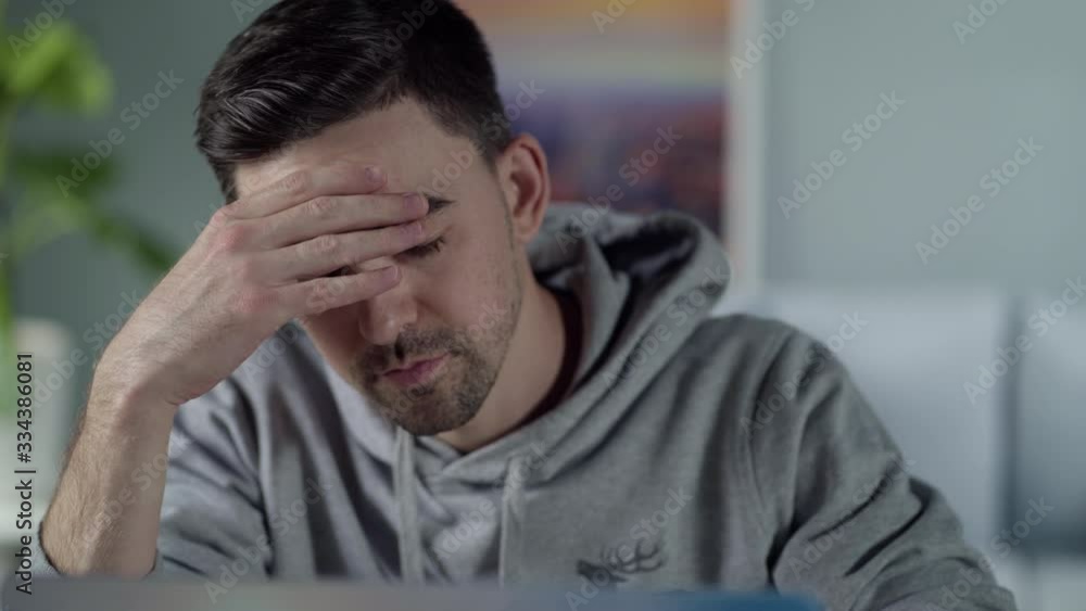 Stay home. Tired young white man is concentrating on the laptop and touches his forehead Stay home. Tired young white man is concentrating on the laptop and touches his forehead