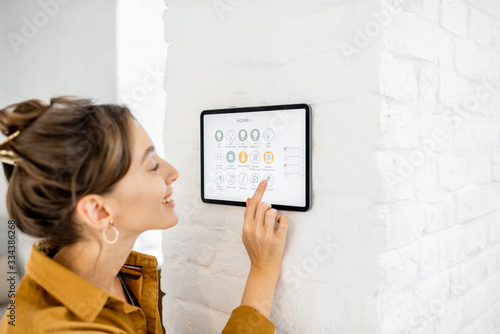 Woman controlling home with a digital touch screen panel installed on the wall in the living room