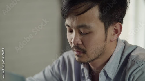 At the close shot sick and tired young Korean man with a mustache and a beard sits at a desk, working on a laptop at home