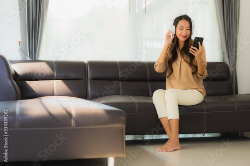 Portrait beautiful young asian woman use smartphone or cellphone on sofa with headphone