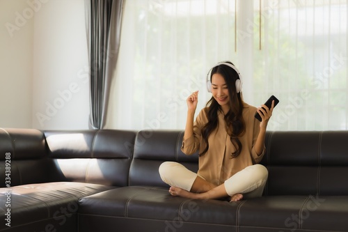 Portrait beautiful young asian woman use smartphone or cellphone on sofa with headphone