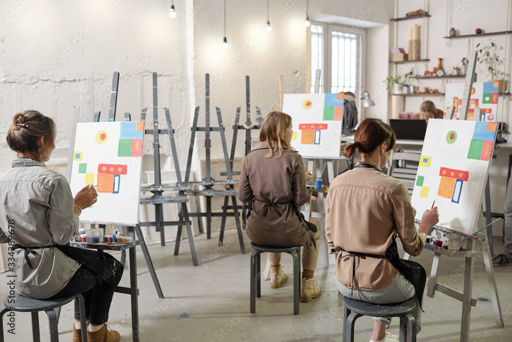 Rear view of female students of painting class sitting in front of easels