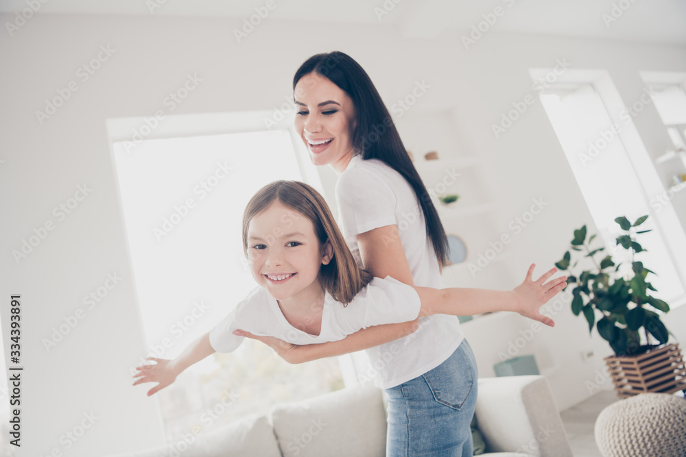 Photo of adorable cheerful positive mom playing with her kid hold hands imagine she fly plane bird stand near couch in living room indoors Photo of adorable cheerful positive mom playing with her kid hold hands imagine she fly plane bird stand near couch in living room indoors