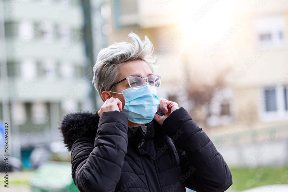Fototapeta premium COVID-19 Pandemic Coronavirus Woman in city street wearing face mask protective for spreading of disease virus SARS-CoV-2. Girl with surgical mask on face against Coronavirus Disease 2019.