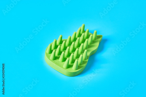Green rubber brush for caring for animal on blue background. Concept of grooming for pet fur