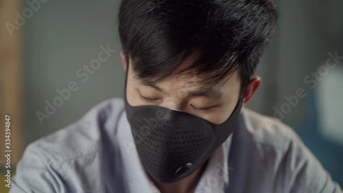 At the close shot young Korean man with face mask sits at a desk, working on a laptop at home