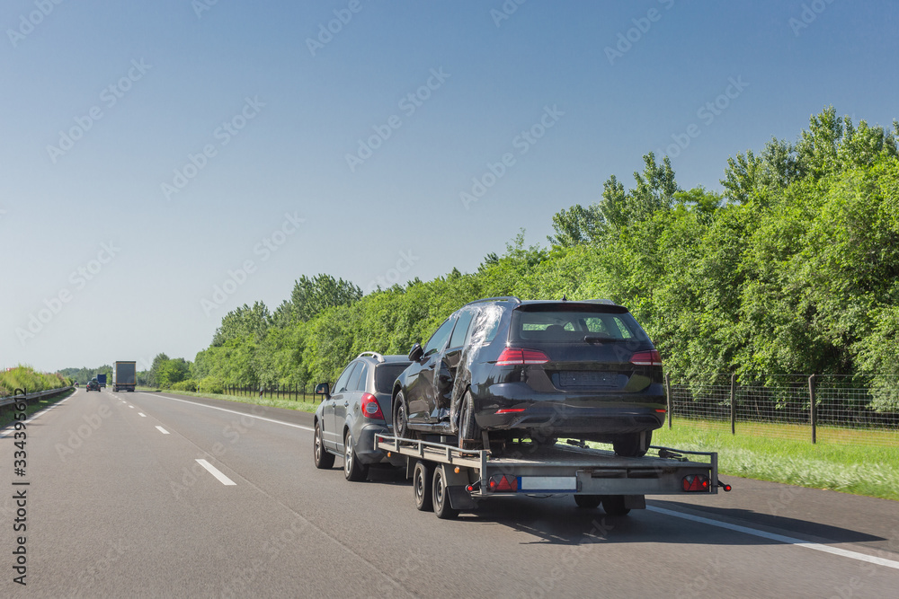 Black broken car after accident on tow truck. Car transported on car carrier trailer on highway