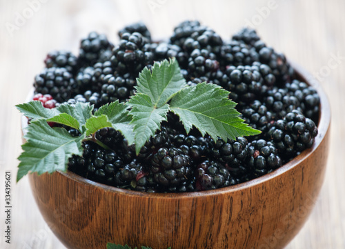 Sweet blackberry and leaves in wooden bowl on wooden table