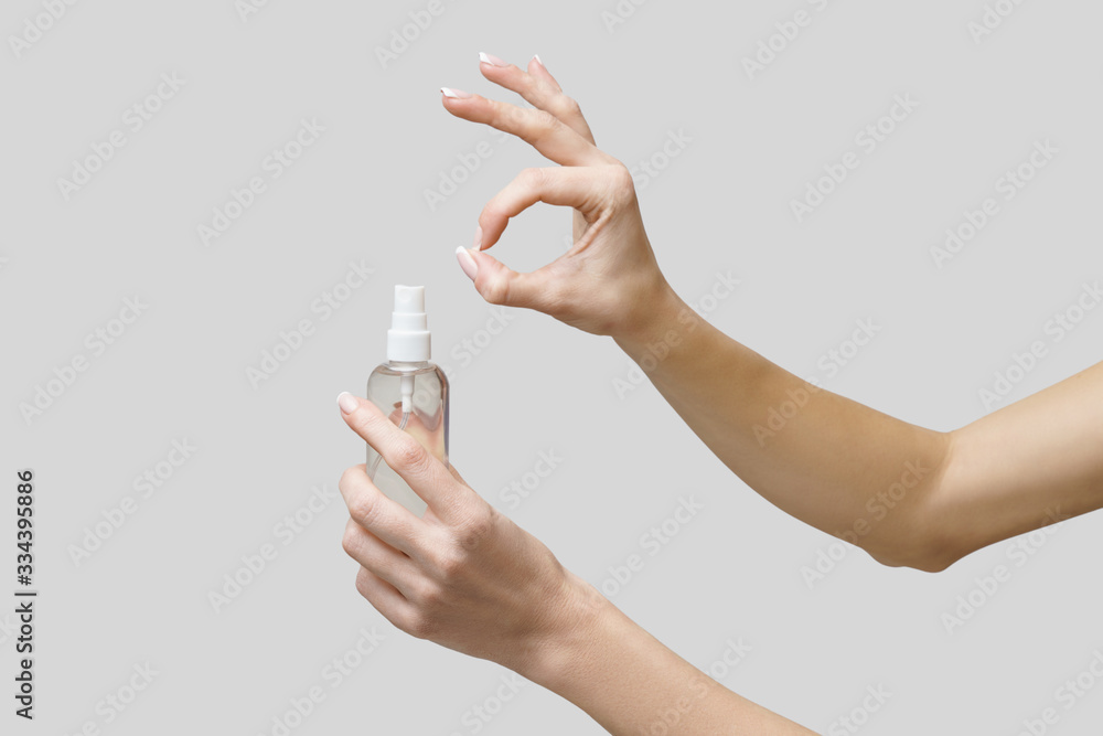 Female hands using hand sanitizer spray dispenser over light grey background Female hands using hand sanitizer spray dispenser over light grey background