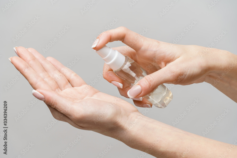 Female hands using hand sanitizer spray dispenser over light grey background - obrazy, fototapety, plakaty 