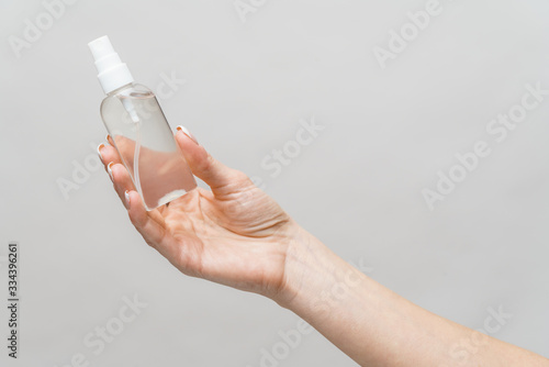 Female hands using hand sanitizer spray dispenser over light grey background