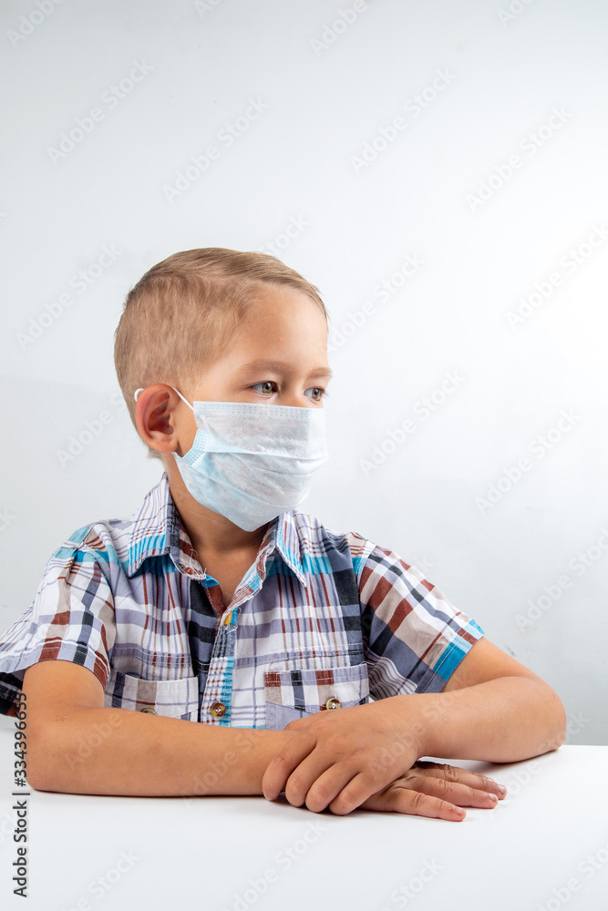 a boy in a medical mask sits at a table, protection during a pandemic from coronavirus a boy in a medical mask sits at a table, protection during a pandemic from coronavirus