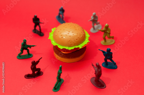 Hamburger surrounded by toy soldiers, burger wars concept or war on fast food concept.