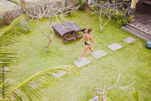Young athletic woman in a bikini walking in green zen garden