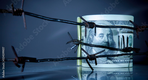 Economic warfare and sanctions concept. US Dollar bills money wrapped in barbed wire.