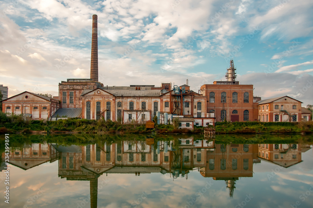 Industrial old building in summer time over blue sky. The old factory building on the lake. Old abandoned factory. Old abandoned building reflected in the water. Space for text.