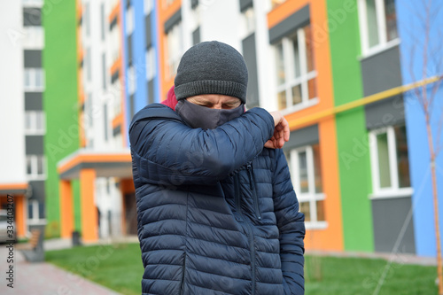 Virus covid-19. Man in medical mask sneezes and coughs on a street in a city in Europe, protects against coronavirus