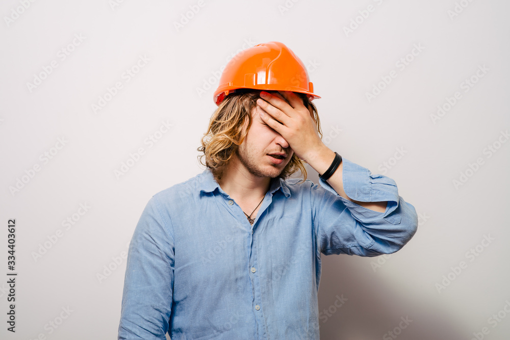 Tired young manual worker - builder, isolated on gray background, close-up studio shot Tired young manual worker - builder, isolated on gray background, close-up studio shot