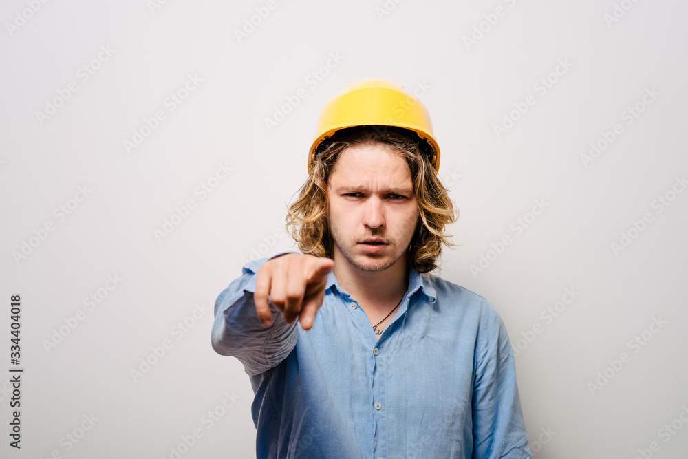 Frowning manual worker - builder, pointing with finger to you or camera, isolated on gray background, close-up studio shot.