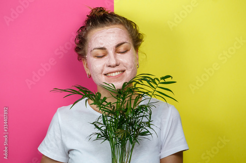 Beautiful young girl with a refreshing mask on her face. Holding a decorative palm in his hands. Beauty and healthy skin