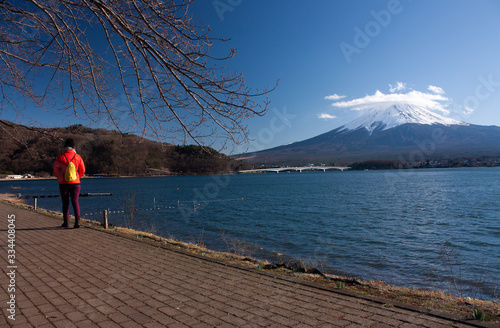 A woman walking near Lake Kawaguchi in Japan, Mount Fuji in the distance on a sunny spring day