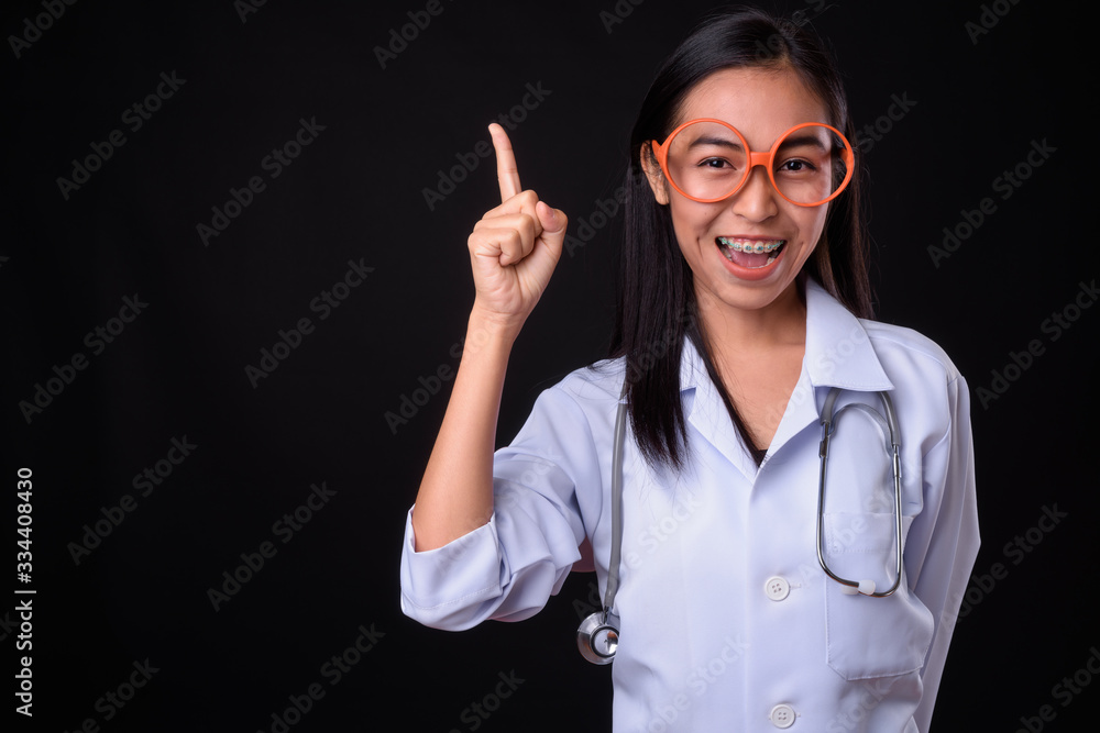 Happy young Asian woman doctor with eyeglasses pointing up Happy young Asian woman doctor with eyeglasses pointing up