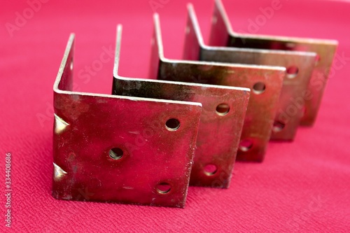 Arrow made of brackets isolated on pink. Metal corners are directed to the left with a place for the text. Golden metal bracket on a red background. Metal corners frames, borders. Isolated. photo