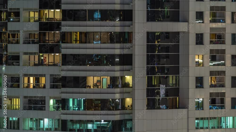 Rows of glowing windows with people in the interior of apartment building at night. Modern skyscraper from glass and concrete. Concept for business and modern life. Pan right Rows of glowing windows with people in the interior of apartment building at night. Modern skyscraper from glass and concrete. Concept for business and modern life. Pan right