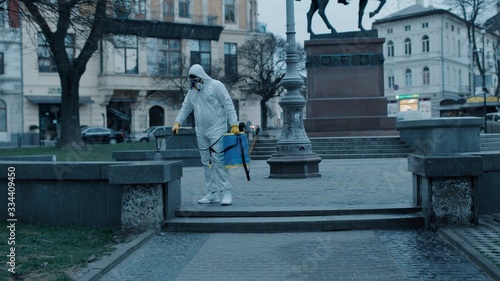 European man in chemical protect wear spray eampty city street with anti bacterial liquid photo