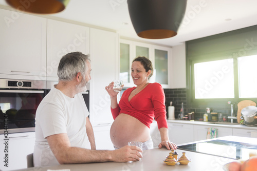 Portrait of happy white Caucasian couple two people, pregnant woman with husband in the kitchen, lifestyle healthy pregnancy happy life concept