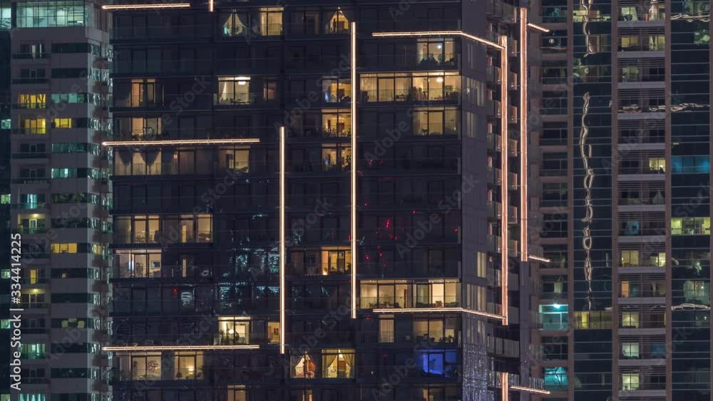 Rows of glowing windows with people in the interior of apartment buildings at night. Modern skyscrapers with glass surface. Concept for business and modern life. Zoom out Rows of glowing windows with people in the interior of apartment buildings at night. Modern skyscrapers with glass surface. Concept for business and modern life. Zoom out