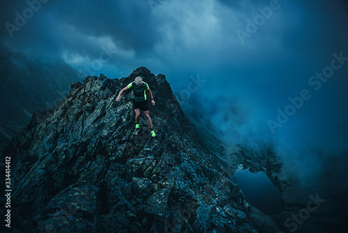 Trail runner in dark evening mountains, rocks. running in storm