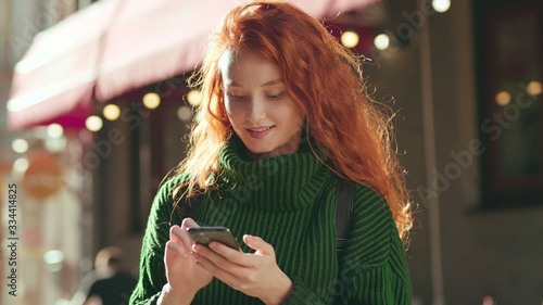 фотографія Portrait of pretty young red hair woman walking down the street smiling using ph