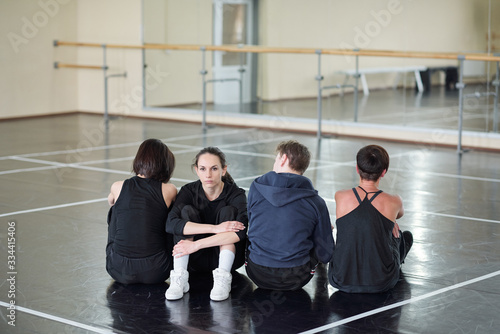 Young serious woman looking at camera while sitting among three dancers