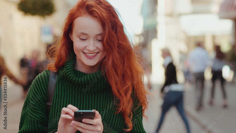 custom made wallpaper toronto digitalAttractive young red hair woman walks down the street uses smartphone chatting texting message smiles and looks around feel happy outside