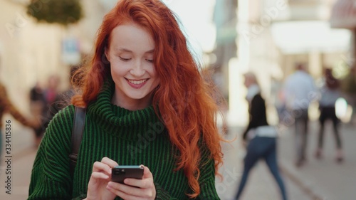 Wallpaper Mural Attractive young red hair woman walks down the street uses smartphone chatting texting message smiles and looks around feel happy outside Torontodigital.ca