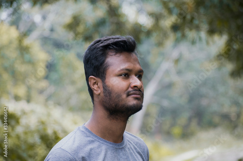 young boy with beard wearing grey t-shirt looking side in front of natural background in a forest garden
