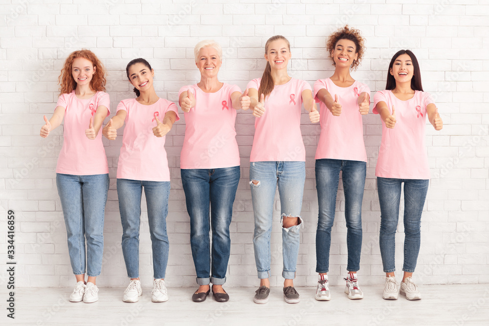 Women In Pink Awareness T-Shirts Gesturing Thumbs-Up Over White Wall Women In Pink Awareness T-Shirts Gesturing Thumbs-Up Over White Wall