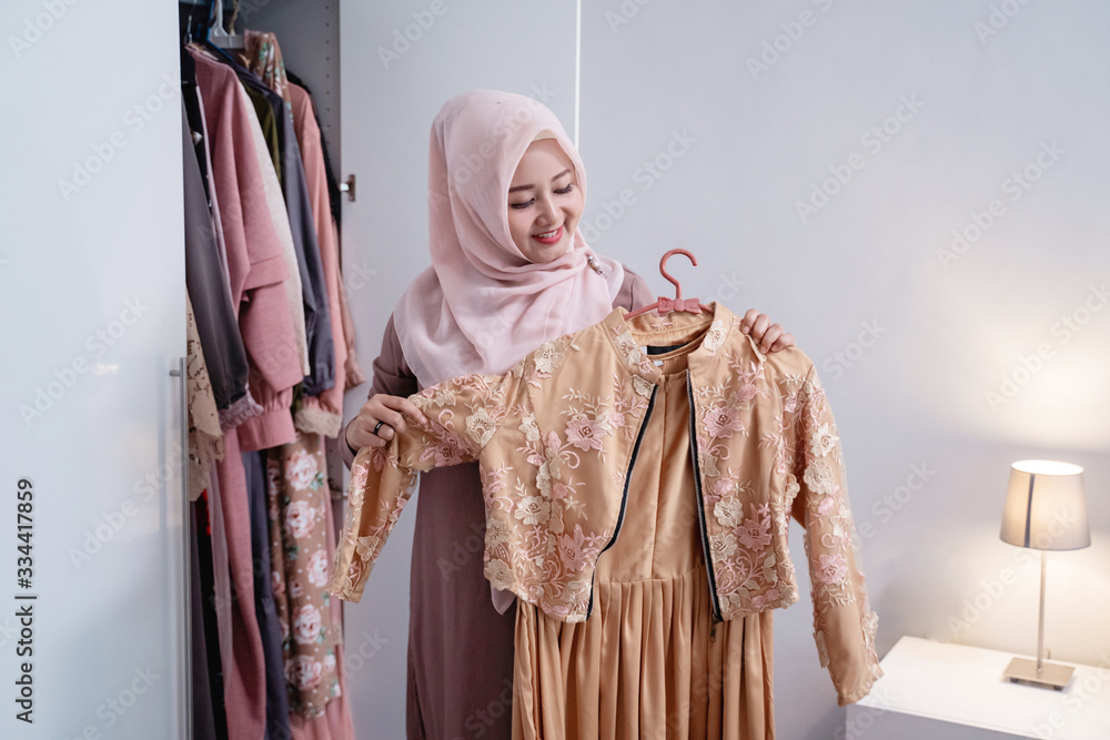 Asian hijab women measure a new gamis by the body in front the wardrobe in the room