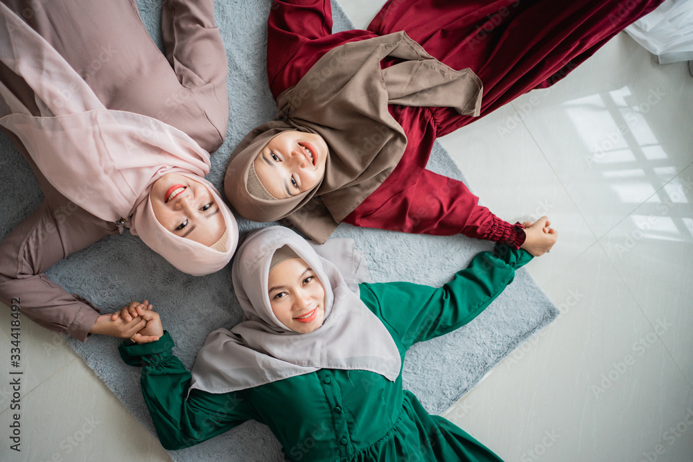 three hijab women smiled while laying on the mattress and holding hands looking up