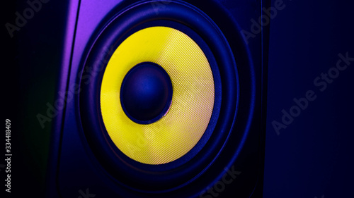 Close-up view of music studio speaker, with a yellow membrane, isolated on a dark blue background, with space for text on the right side. Electronic music concept