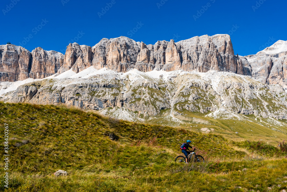 Radfahrer fährt durch eine Wiese mit Blick auf die Sellagruppe der Dolomiten