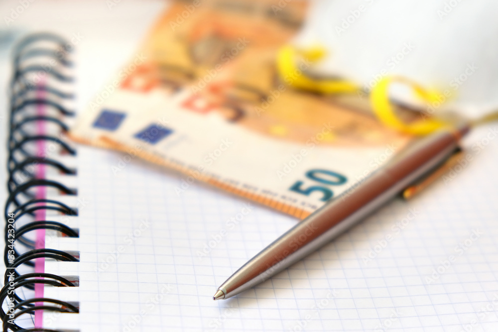 Luxury Pen, Protective mask and 50 Euro bank notes on a white paper copybook background. Luxury Pen, Protective mask and 50 Euro bank notes on a white paper copybook background.
