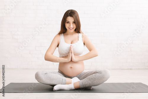 Active pregnant woman meditating in lotus position at home