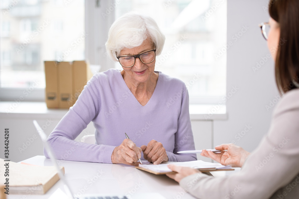 Senior client putting her signature in insurance agreement after consulting Senior client putting her signature in insurance agreement after consulting