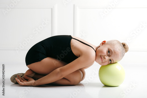 Quadro su tela Young girl athlete rhythmic gymnastic in a black suit lyong on the floor, head o