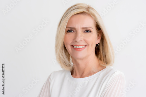 Headshot of blond senior woman while standing at isolated white background © sepy